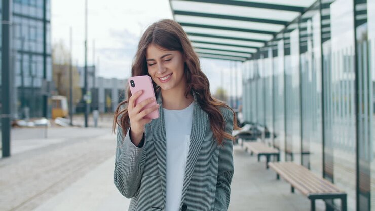 Young woman smiling while using her smartphone at a bus stop