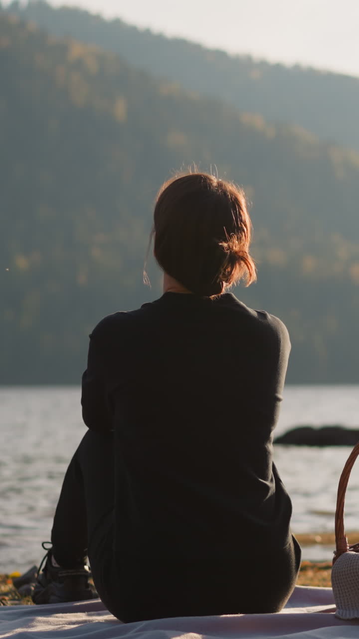 mujer disfruta de la vista panorámica en el picnic. relajarse en la orilla con vistas a las montañas onduladas con densos bosques. dama solitaria admirando la belleza de la naturaleza sentada en cuadros con canasta de comida