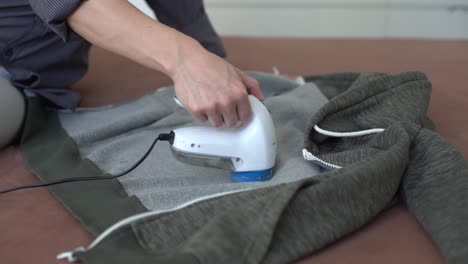 woman uses a machine for removing pellet and spools from clothes and fabric on black trousers. a modern electronic device for updating old things.