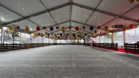 little girl skating on ice alone in empty indoor ice rink with christmas decoration balls hanging on ceiling