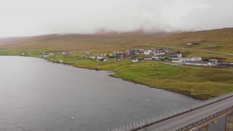 Vista-Aérea-Sobre-El-Fiordo-Y-El-Puente-Hacia-Un-Pequeño-Pueblo-En-Las-Islas-Feroe