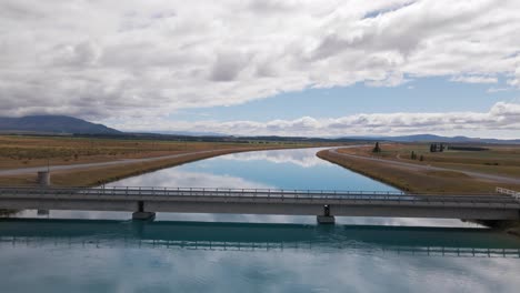 Van-crossing-a-narrow-bridge-over-a-crystal-clear-blue-river-in-rural-New-Zealand