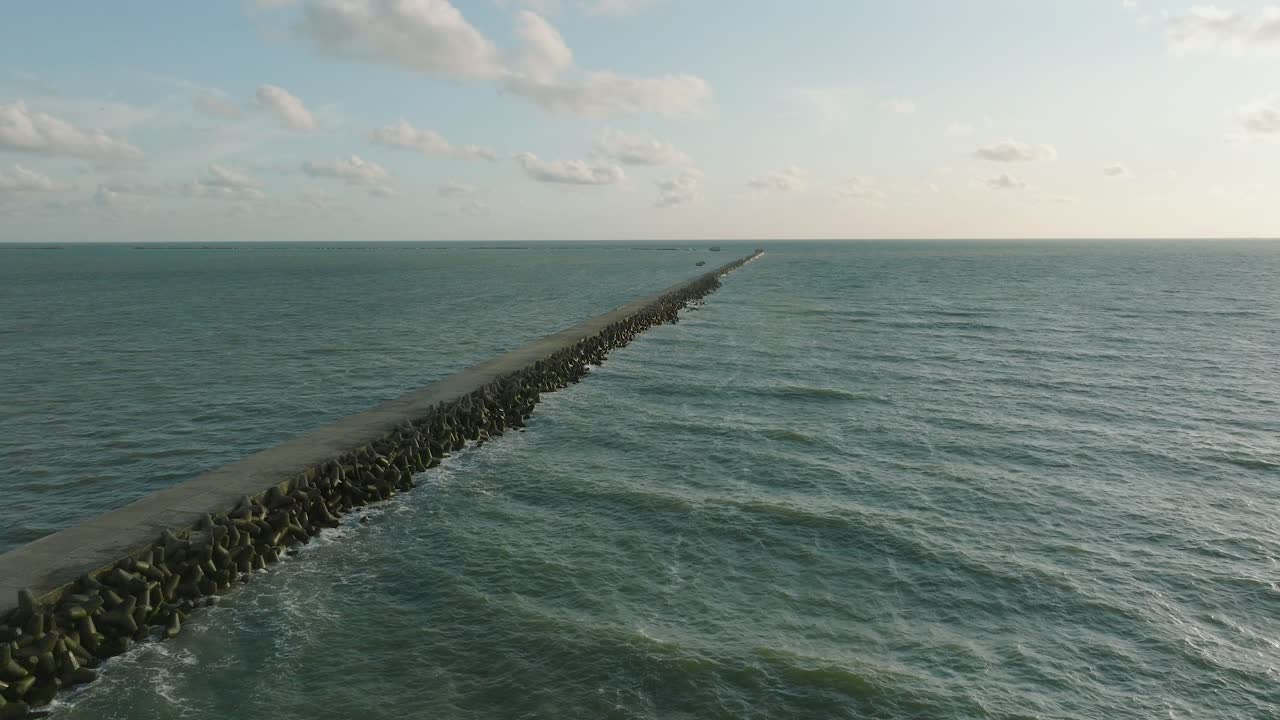 Aerial establishing view of Port of Liepaja concrete pier, Baltic sea coastline , sunny day summer evening, golden hour light, big waves splashing, wide drone dolly shot moving right