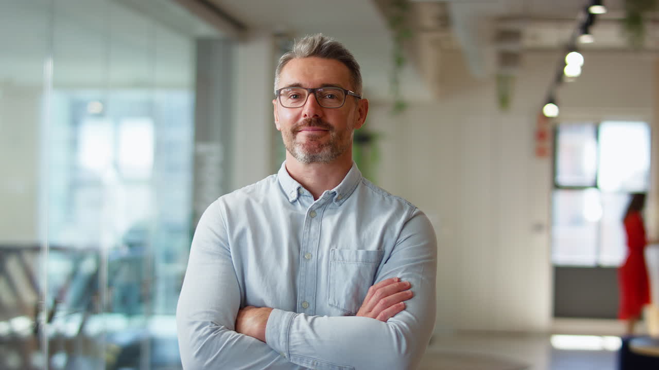 Portrait Of Serious Mature Businessman Wearing Glasses  Standing In Modern Open Plan Office