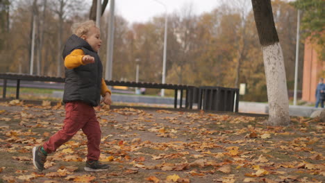 funny little boy is running in park area at autumn day having fun at walking at weekend active rest of family in city at fall season