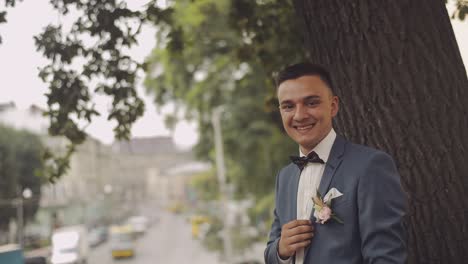 Un-Novio-Guapo-Se-Queda-Cerca-De-Un-árbol-En-La-Calle-De-La-Ciudad.-Día-De-La-Boda