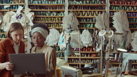 women working on laptop and talking in shoemaking workshop