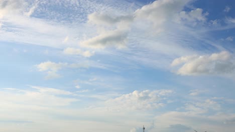 calm cloud blanket forming and small cumulus clouds passing by with a blue sky and sun rays into sunset