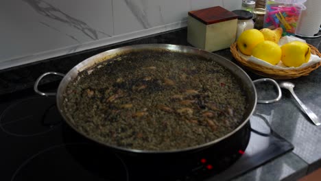 Yellow-apples-arranged-in-basket-beside-paella-dish-being-prepared-with-black-squid-ink