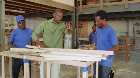 arriving at workbench black male foreman instructing assistants stacking wooden planks for order