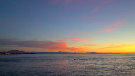 Filmische-Atemberaubende-Noch-Dramatische-Leuchtend-Orangefarbene-Wolken-Sonnenuntergang-Abenddämmerung-Boot-In-Der-Bucht-Leuchtturm-Biarritz-Hossegor-Frankreich-Strand-Berg-Küstenlandschaft-Biarritz-Baskenland-Stadtlichter-Ruhiges-Wasser