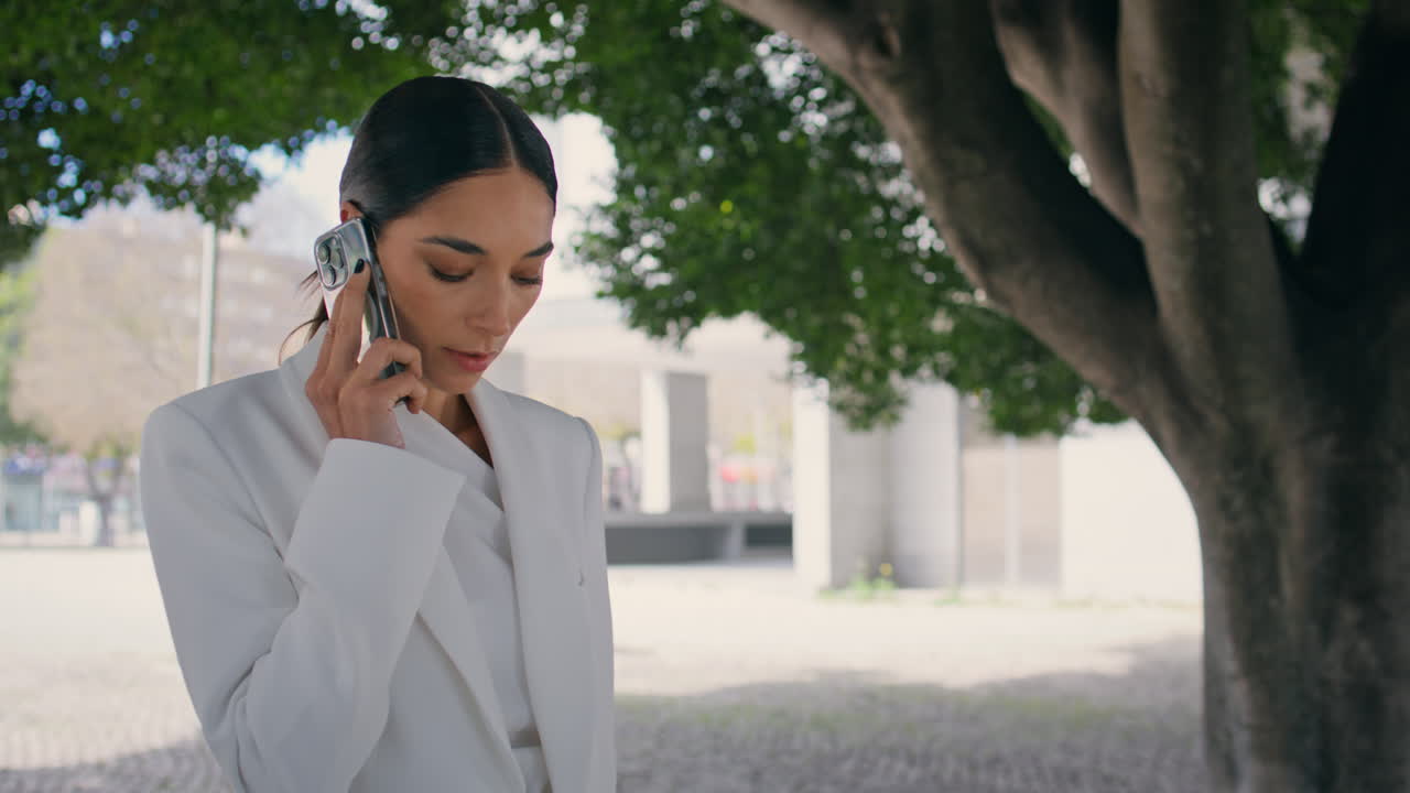 여성 사업주가 나무 에 서서 전화를 하고 있습니다. 소녀가 전화로 이야기하고 있습니다.