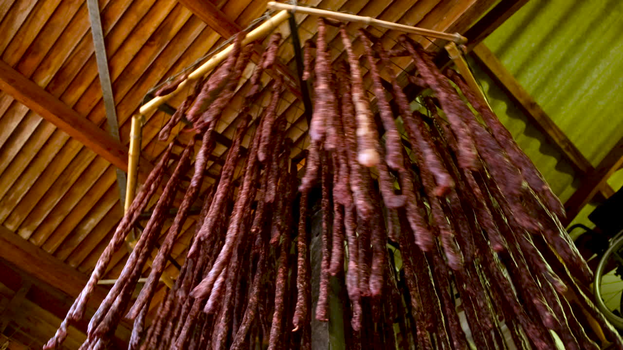 Numerous sausages or cured meats hanging from a wooden ceiling structure