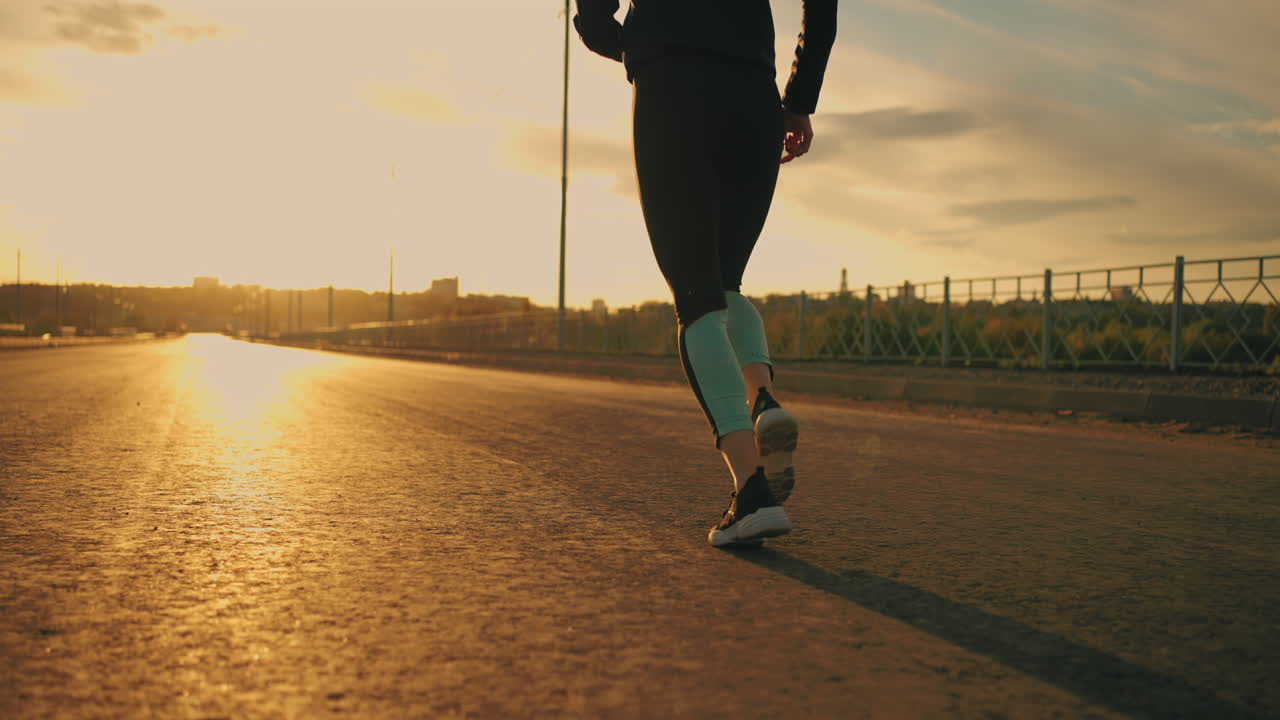 professional female runner is training outdoors in sunset or sunrise rear view of legs woman is jogging