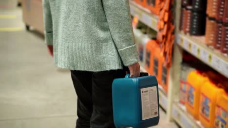 A-woman-walking-by-hardware-store-with-plastic-canister-in-hands,-rare-view