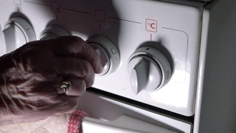 hands of elderly lady turning on oven at dial close up shot