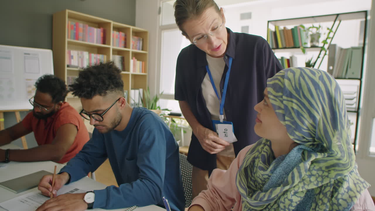 Female Teacher Helping Girl in Hijab during Exam in School for Immigrants