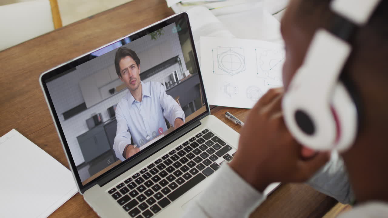 African american businessman sitting at desk using laptop having video call with male colleague