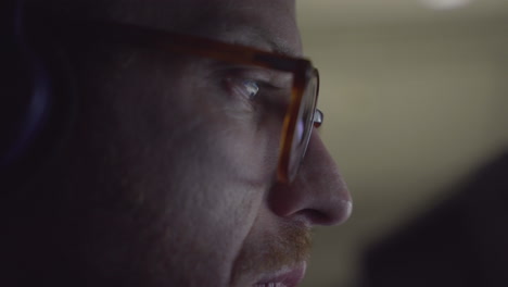 man wearing glasses focused on screen of computer or smartphone