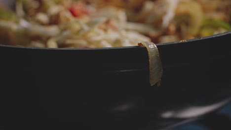 slice of onion hanging off the edge of a wok with vegetables inside of it