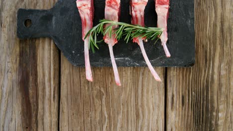 chuletas de carne cruda y romero dispuestas en la bandeja de piedra