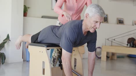 Hombre-Caucásico-Senior-Enfocado-Haciendo-Ejercicio-Con-Una-Entrenadora-De-Pilates,-Inalterada,-En-Cámara-Lenta