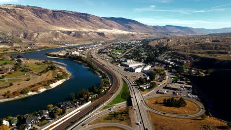 drone pan right aerial shot of bridges,highway 1 and yellowhead highway in the city of kamloops bc canada,train,trucks, the thompson river on a cloudy day in a desert environment