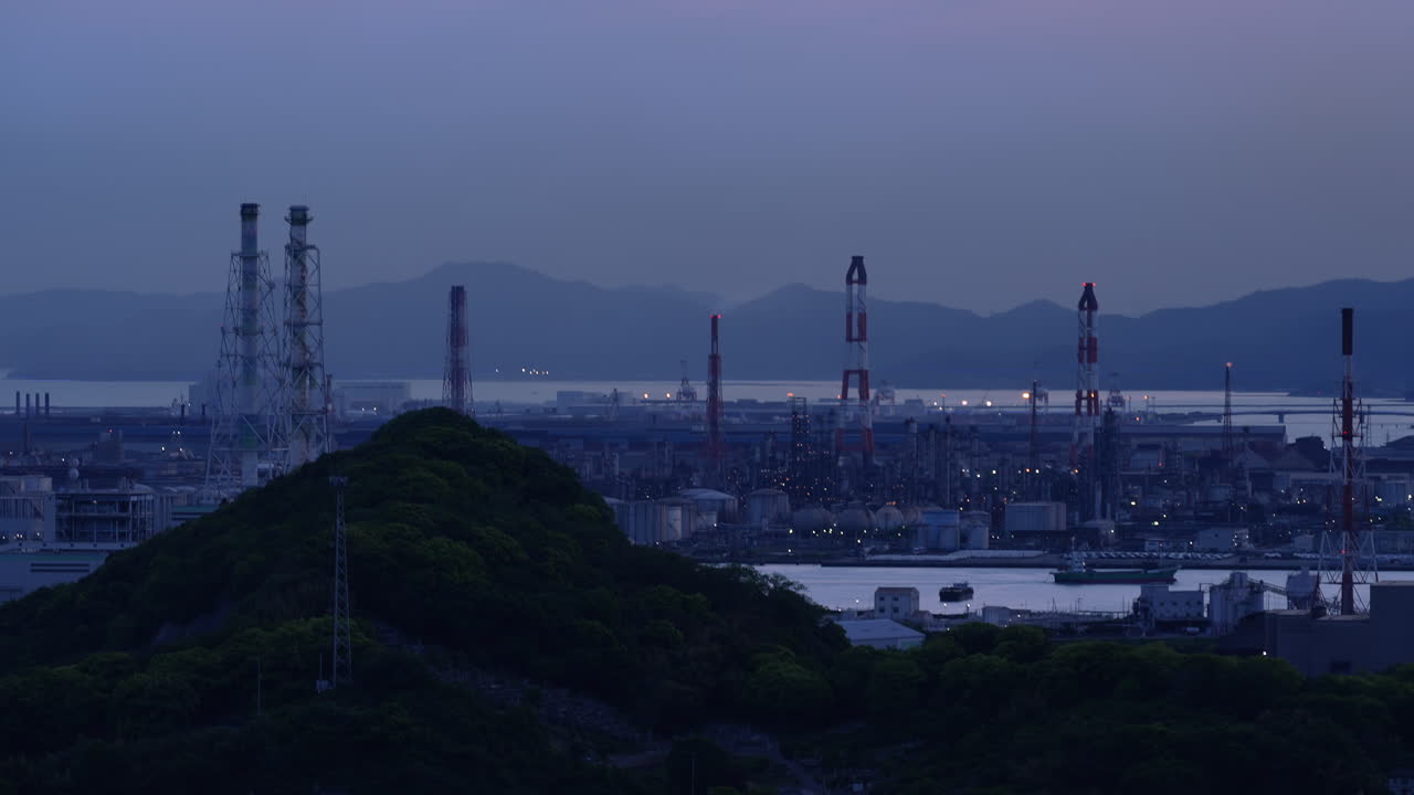Industrial plant with smoking chimneys and burning flare stacks at dusk