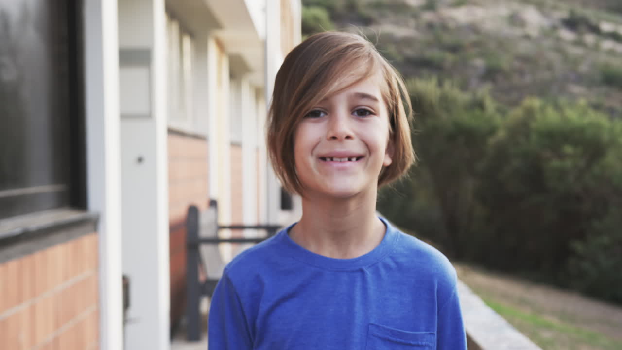 Standing outside school building, smiling boy wearing blue shirt