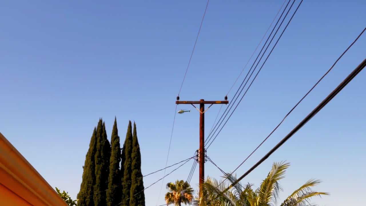 Police helicopter flying by some trees and powerlines with blue sky and no clouds.