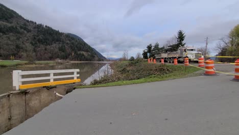 a heavy truck with a trailer drives around the river and the hill in the background on a cloudy day, abbotsford, bc, canada - gimbal shot