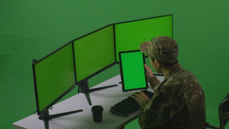 side view of asian man soldier working with tablet and multiple computer monitor with mock up green screen in green screen studio