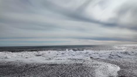 panning shot of sandy beach is softly caressed by a gentle sea wave, envelops the scene in a sense of stillness, black sand beach