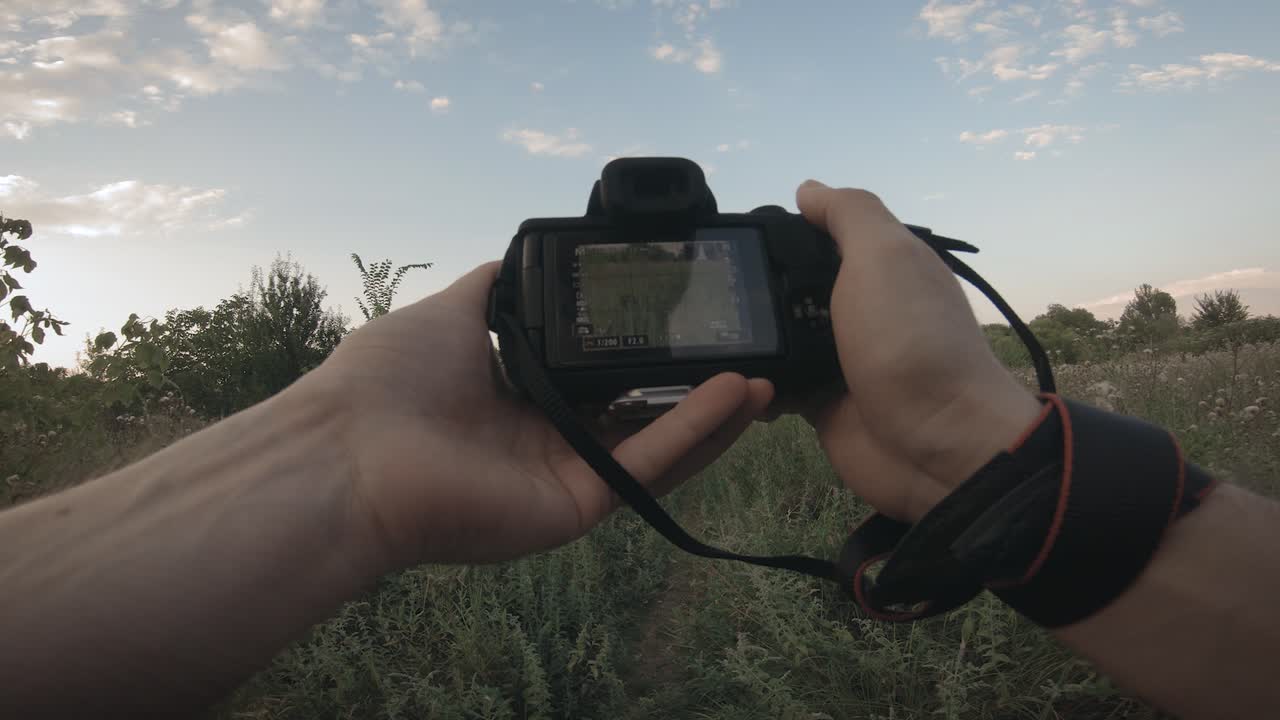GoPro action camera POV shot when opening a mirrorless photo camera in a field of tall grass with some puffy white clouds in the sky