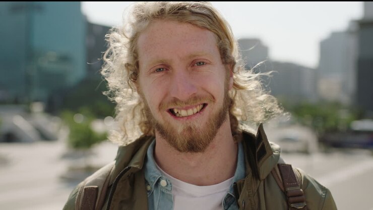 ritratto di un giovane uomo biondo barbuto studente che guarda la telecamera sorridendo felice allegro godendo di uno stile di vita urbano soleggiato