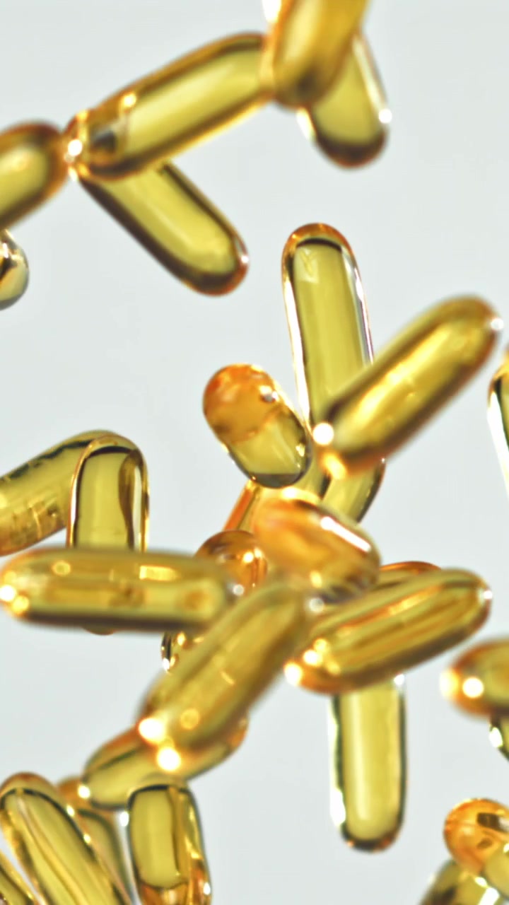 Capsule Softgel Dorate che Cadono al Rallentatore su Sfondo Bianco.