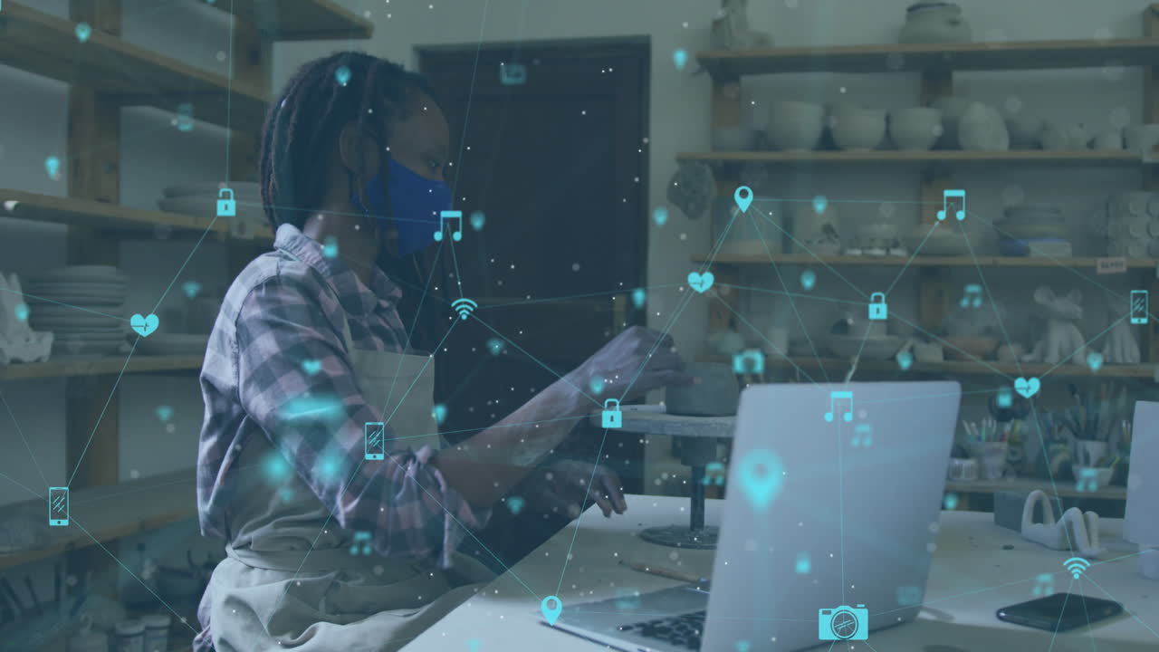 Animation of network of connections over african american woman with face mask doing pottery