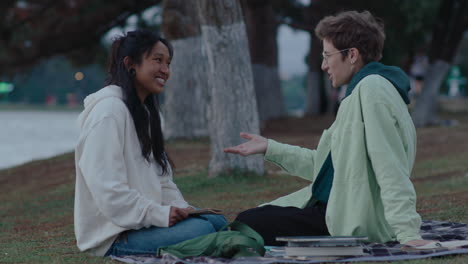 two girlfriends sitting on grass chatting in the park