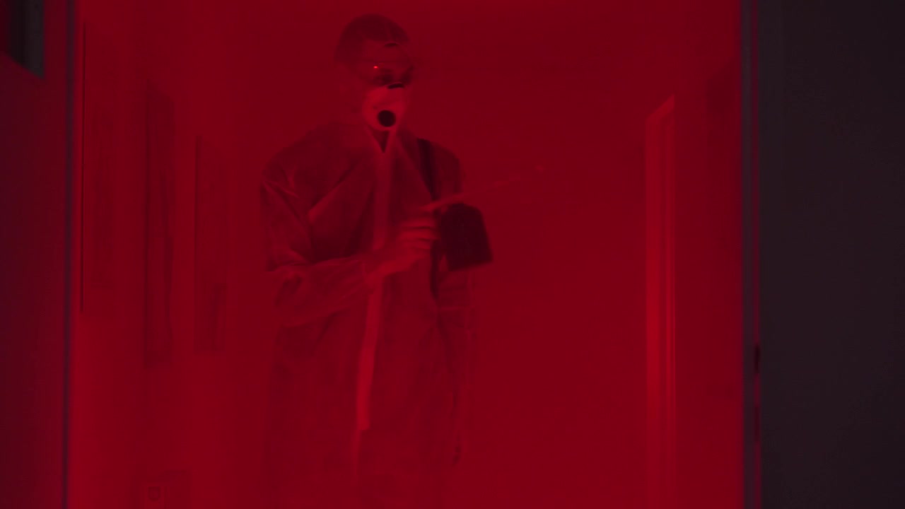 Specialist in protective suit in long hazy corridor sprays disinfectant liquid on walls