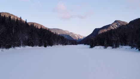 Aerial-flight-over-snow-covered-river-flowing-from-fjord-through-boreal-forest-in-Parc-National-de-la-Jacques-Cartier,-Quebec-Canada