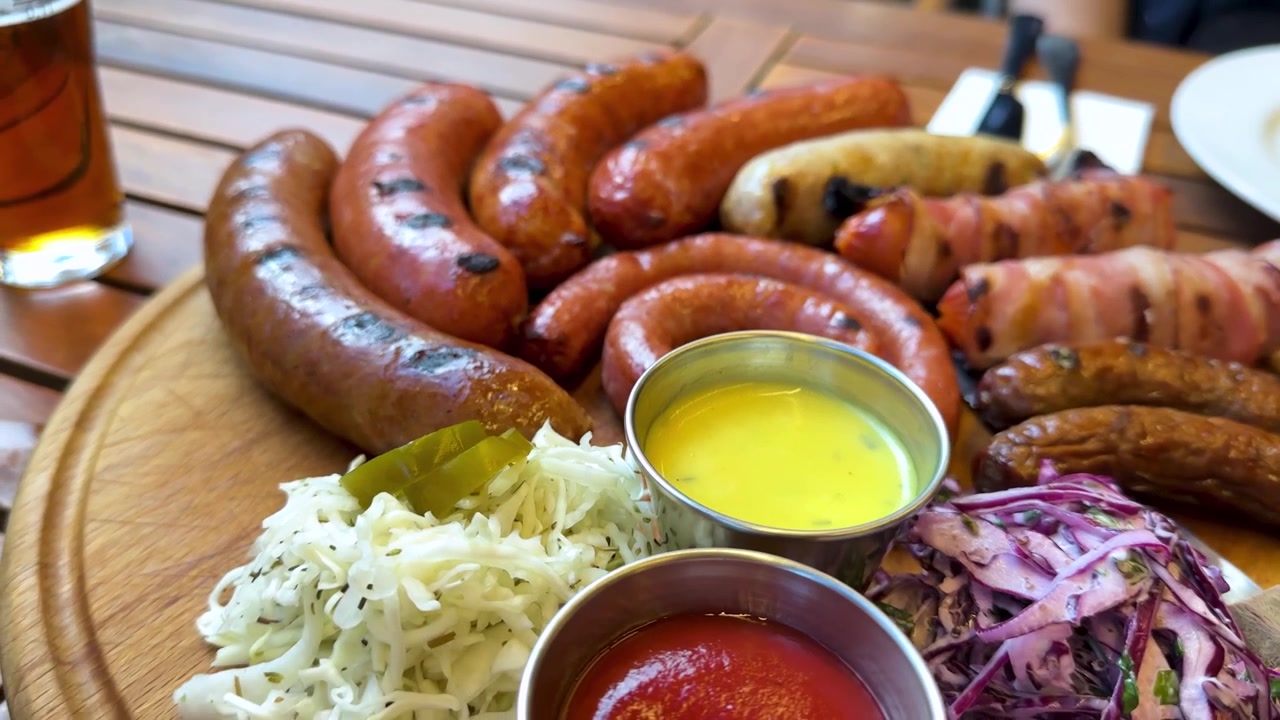 Deliciosa cocina caucásica con salchichas artesanales a la parrilla, chorizo y tocino a la barbacoa, servidos en una tabla de madera para picnic. Salsa, encurtidos, ensalada, cerveza. Hospitalidad rústica, reunión veraniega ahumada, comida tradicional.
