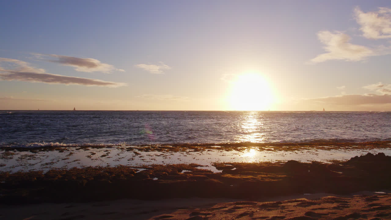 Tomada panorâmica para a esquerda através do vasto Oceano Pacífico, do sol poente branco e brilhante até a costa sombria, revelando o brilho alpino rosado pouco antes do pôr do sol em Oahu, Havaí