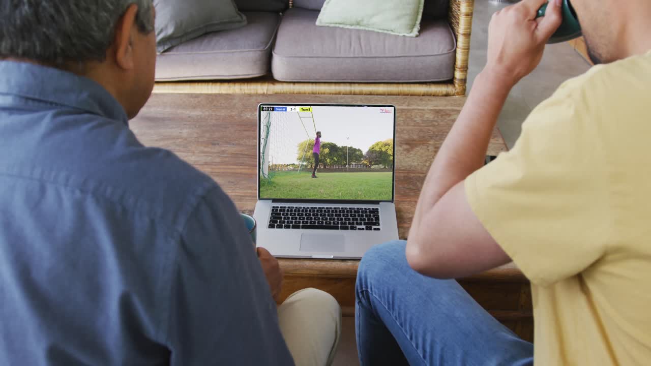 Vídeo de pai e filho sentados no sofá assistindo a um jogo de futebol no laptop