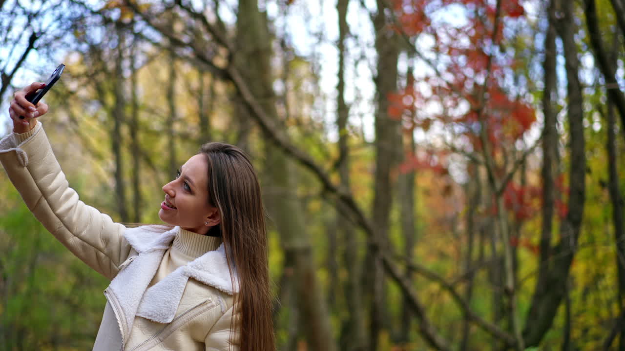 Attractive long-haired brunette taking selfie on her phone. Lady taking picture of herself in the autumn nature. Blurred backdrop.