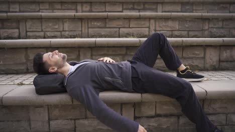 Happy male student lying on the floor outdoors resting, relaxing.