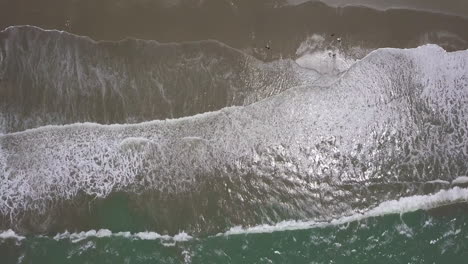 cenital drone shot flying straight down over the splashing waves at the beach in playas general villamil, ecuador