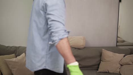 Enfeebled-young-handsome-man-falling-down-on-a-couch-after-cleaning,-feeling-tired-after-washing-wooden-floor.-Exhaling.-Wearing-green-rubber-gloves.-Slow-motion