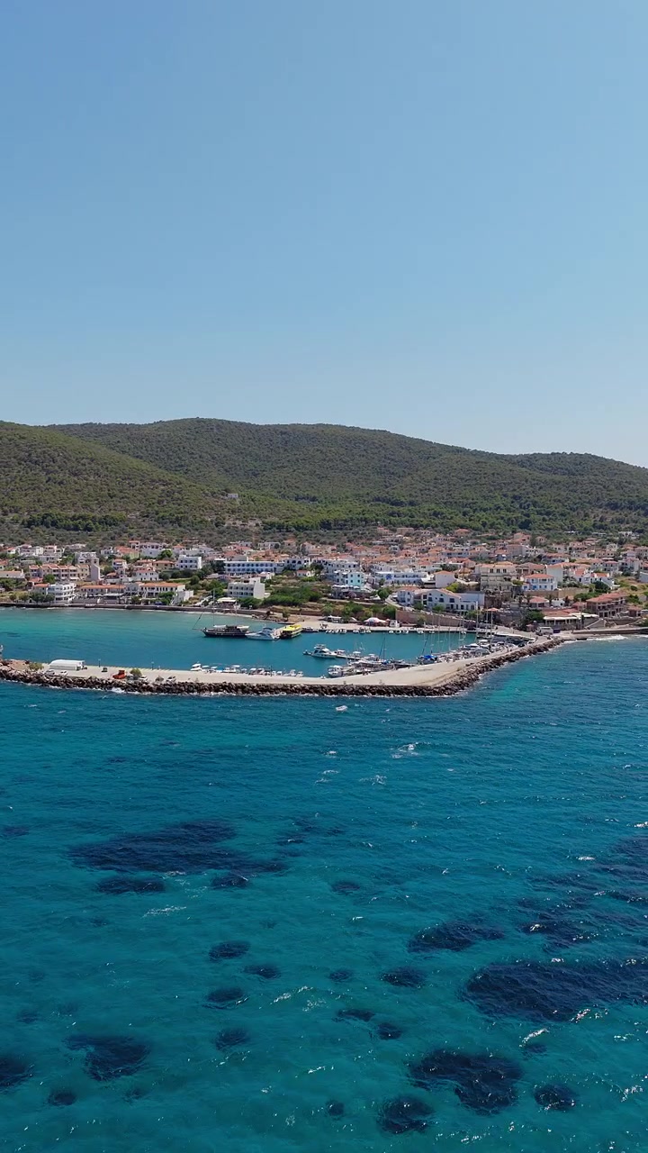 Vertikal panoramisk drönarbild över byn Megalochori och dess hamn, på ön Agistri, Grekland. Kristallklart vatten, solig sommardag, molnfri himmel