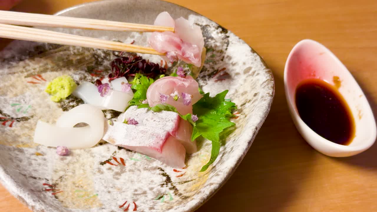 Le bacchette prendono pesce crudo da un piatto di ceramica con foglia di shiso e wasabi