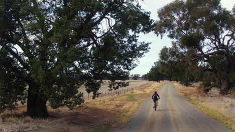 drone following female mountain biking along country dirt road in rural australia